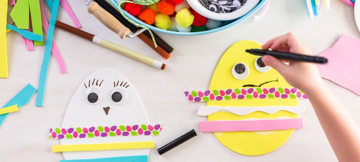 Image shows a childs hand holding a pen. They are about to draw on a paper egg. 