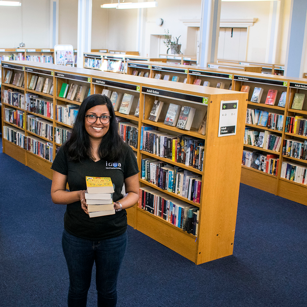 member of staff holding a pile of books inside Cubitt Town Library