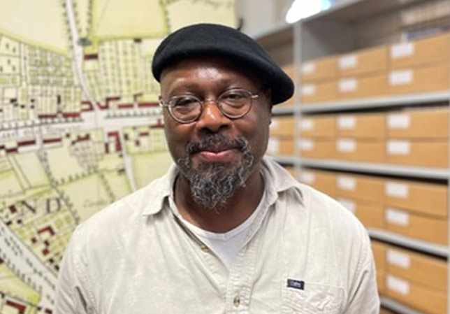 Portrait of Tony T standing in front of shelves in the public reading room